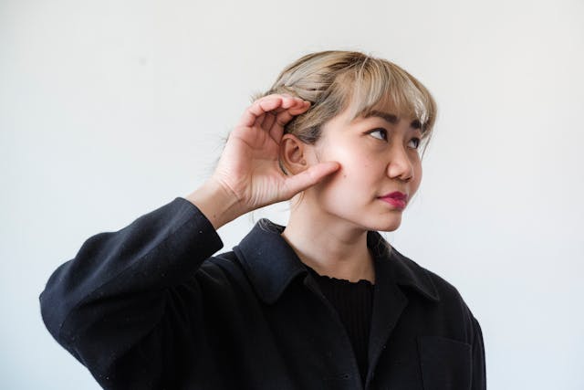 een vrouw die haar hand achter haar oor houdt, alsof ze beter probeert te luisteren.